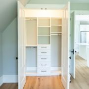 A white closet in an attic with wooden floors featuring custom closet design.