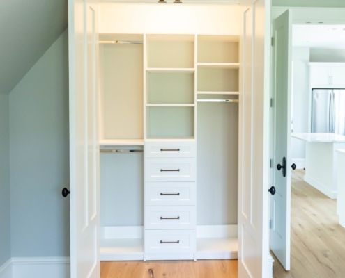 A white closet in an attic with wooden floors featuring custom closet design.